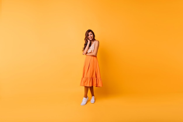 Fulllength photo of appealing woman in long orange skirt Lovely caucasian female model in summer attire spending time in studio