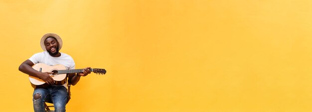 Free photo fulllength photo of excited artistic man playing his guitar isolated on yellow background