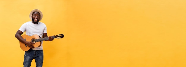 無料写真 黄色の背景に分離されたカジュアルなスイートでギターを弾く興奮した芸術的な男性の全身写真