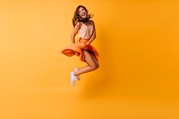 Fulllength photo of tanned ginger girl jumping on yellow background and smiling Adorable young woman in trendy summer clothes fooling around in studio