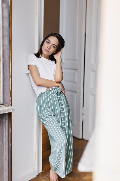 Fulllength portrait of romantic brunette girl in pajamas chilling at home Indoor shot of charming woman relaxing during rest in her apartment