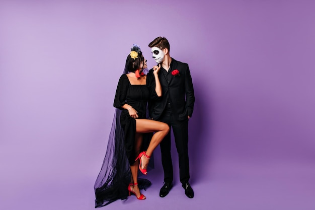 Fulllength portrait of zombie girl in high heel shoes posing with boyfriend Loving couple in muertos costumes celebrating halloween