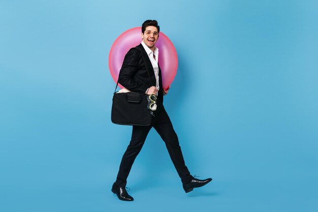 Fulllength shot of man in black suit and white shirt on blue background Brunette guy with smile poses holding inflatable circle