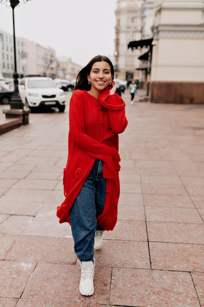 Fulllenhgt portrait of stylish pretty woman with dark hair and great smile is wearing long red knitted coat