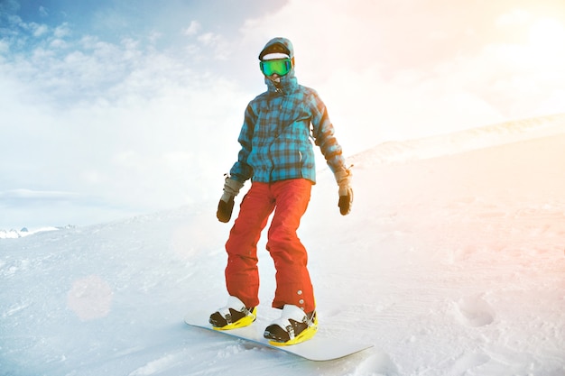 추운 초보자부터 완벽하게 장착 된 스노우 보더가 Google 마스크를 쓰고 뒤쪽 가장자리의 스키장 꼭대기에 홀로 서 있습니다.