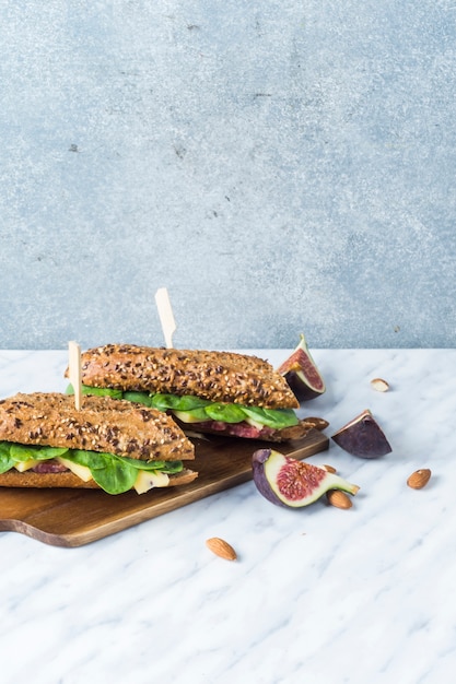 Fully loaded hot dogs on chopping board with fig slices and almonds over white marble backdrop