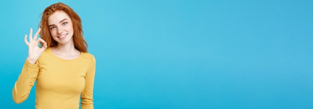 Бесплатное фото fun and people concept headshot портрет очаровательной рыжеволосой рыжеволосой девушки с веснушками, улыбающейся и делающей знак пальцем пастельно-синий фон copy space