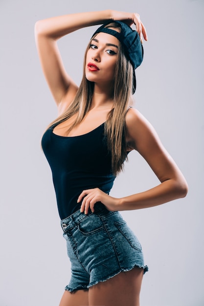 Funky style beauty. Portrait of beautiful young woman in glasses and funky hat while standing against grey wall