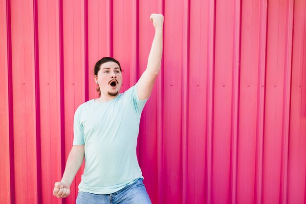 Funniest young man clenching his fist against pink corrugated metal backdrop