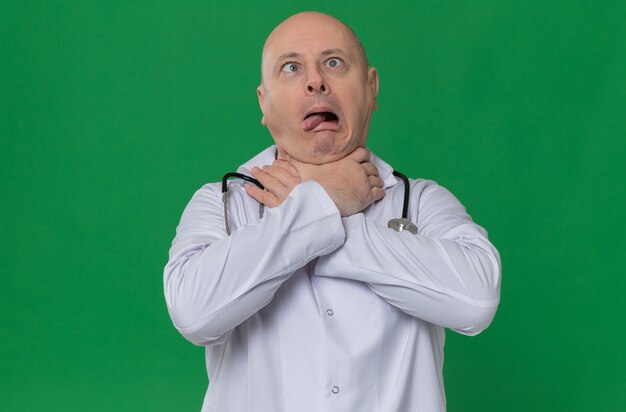 Funny adult slavic man in doctor uniform with stethoscope choking himself with hands