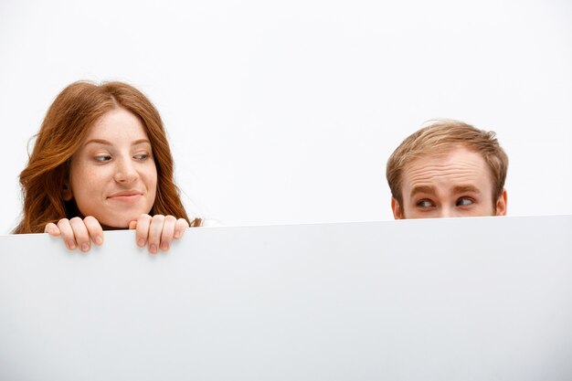 Funny adults redhead man and woman hiding behind table