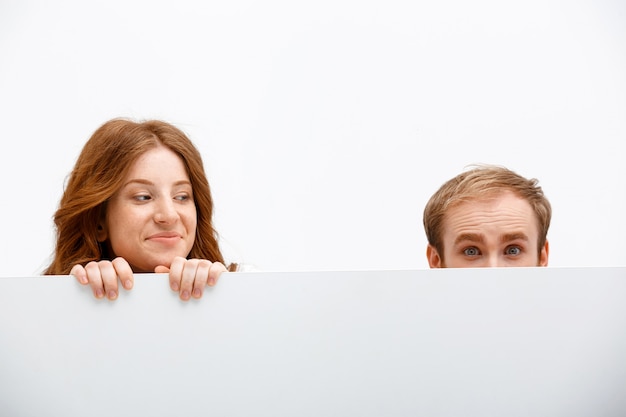 Funny adults redhead man and woman hiding behind table