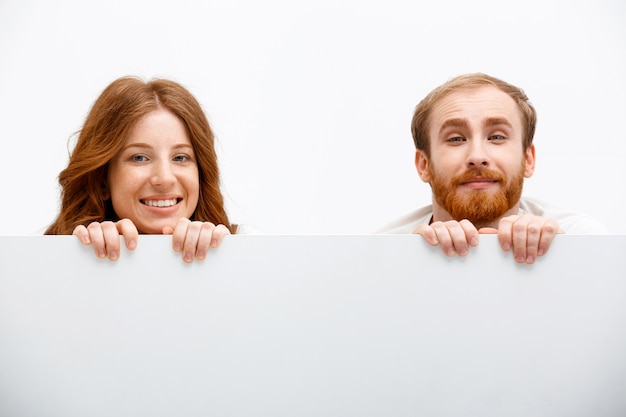 Funny adults redhead man and woman hiding behind table