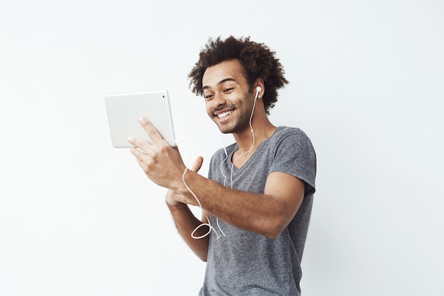 Funny african man in headphones laughing looking at tablet.