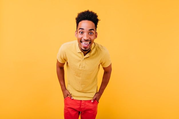 Free photo funny african model in bright red pants posing with hands in pockets. pleased black guy standing with sincere laugh.