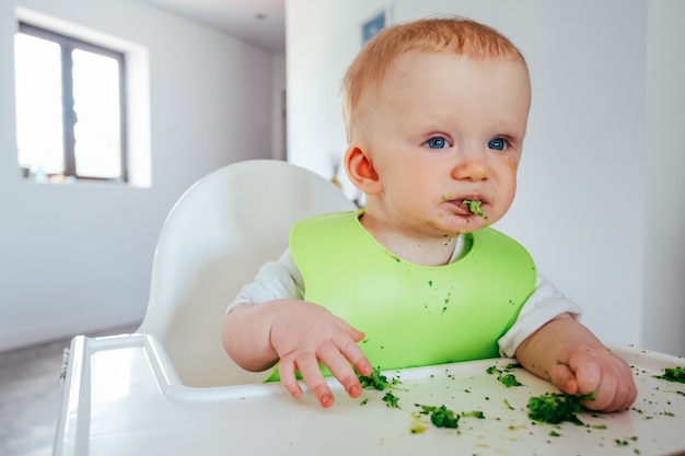 Funny baby girl eating soft cooked vegetables by herself