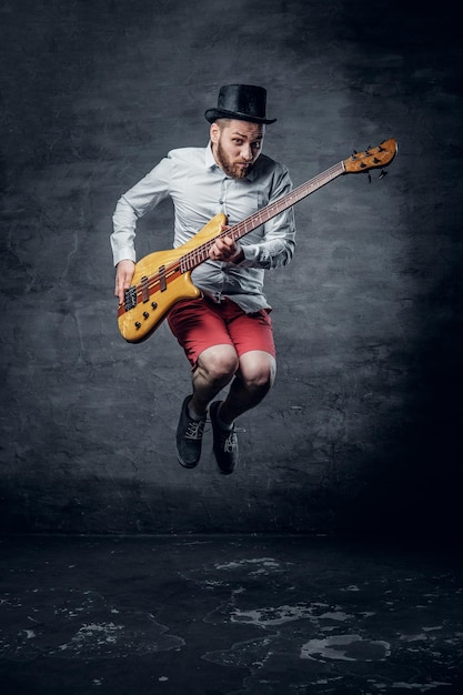 Free photo funny bass player in a jump dressed in a cylinder hat.