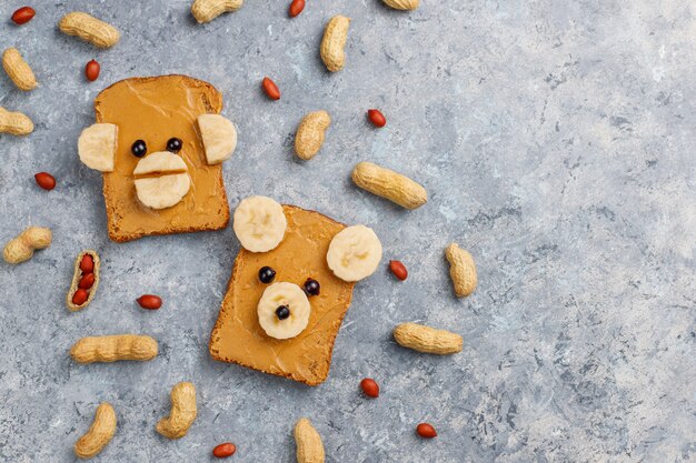 Смешной медведь и обезьяна лицо бутерброд с арахисовым маслом, бананом и черной смородиной, арахис на сером фоне бетона