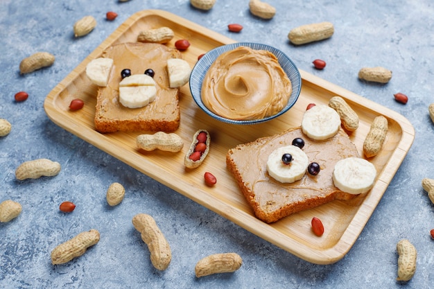 Funny bear and monkey face sandwich with peanut butter, banana and black currant, peanuts, top view