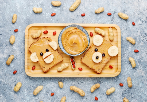 Free photo funny bear and monkey face sandwich with peanut butter, banana and black currant, peanuts, top view