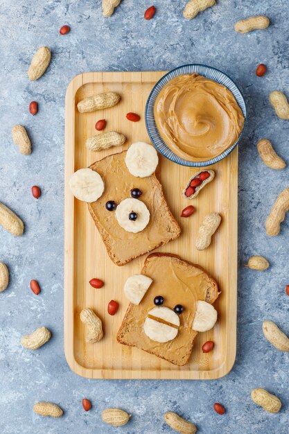 Funny bear and monkey face sandwich with peanut butter, banana and black currant, peanuts, top view