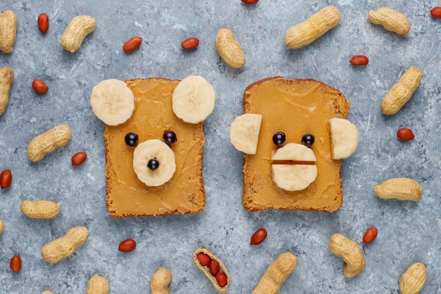 Free photo funny bear and monkey face sandwich with peanut butter, banana and black currant, peanuts, top view