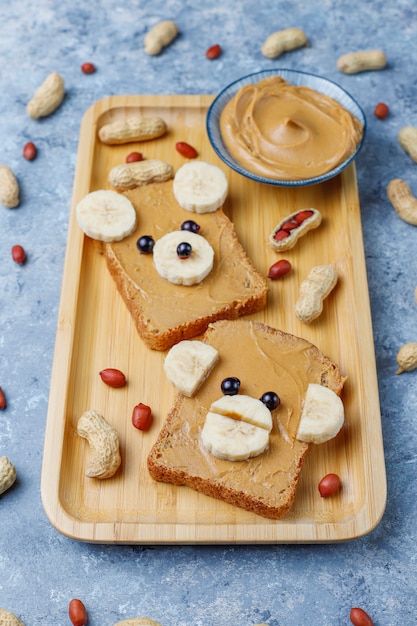 Funny bear and monkey face sandwich with peanut butter, banana and black currant, peanuts, top view