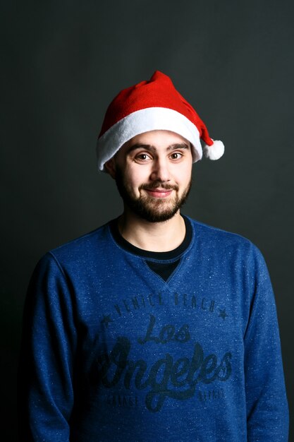 Забавный бородатый мужчина в красной рождественской шляпе пересекает руки на груди