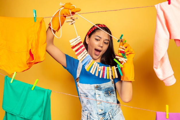 Funny and beautiful housewife doing housework on yellow background