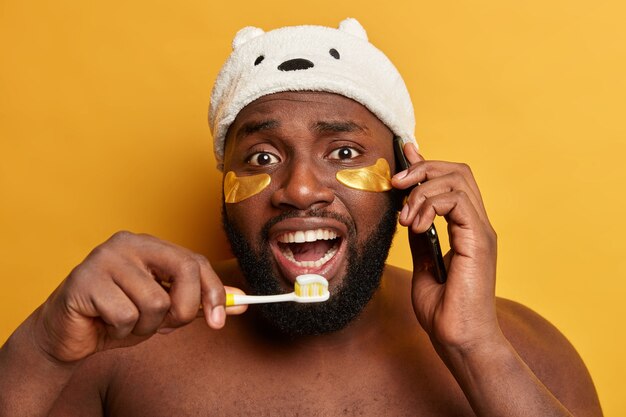 재미있는 흑인 남자는 치아를 걱정하고, 치약으로 칫솔을 들고, 잔주름을 줄이기 위해 콜라겐 패치를 착용합니다.
