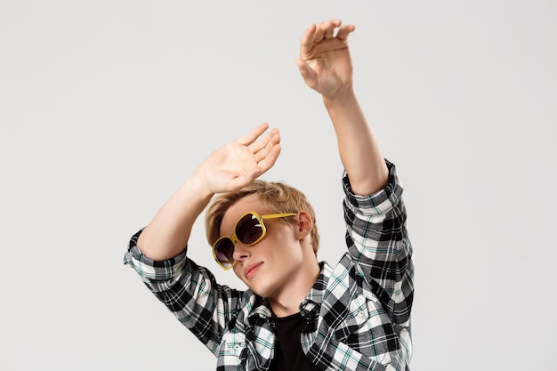 Free photo funny blond handsome young man wearing sunglasses and casual plaid shirt dancing waving hands the air