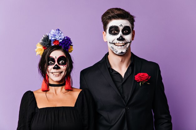 Funny boy and girl with faces painted in mexican style are looking at camera in surprise and smiling.