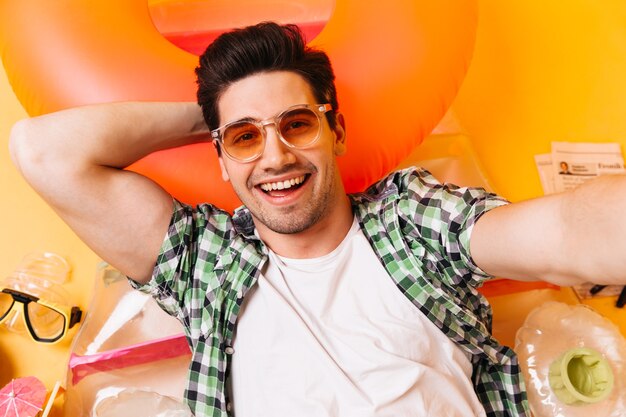 Funny brunette man in white T-shirt and glasses makes selfie on inflatable mattress.