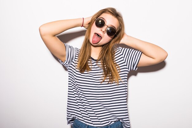 Funny casual teenager woman wearing fashion sunglasses gesturing isolated on a white wall