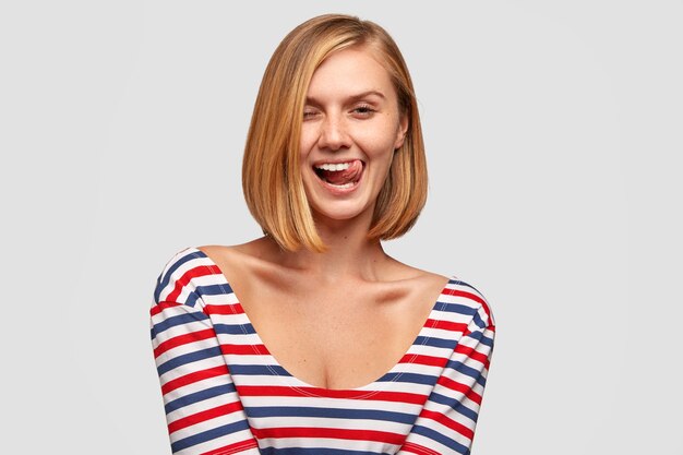 Funny Caucasian girlfriend has joy, smiles broadly, shows tongue, has bobbed hairstyle