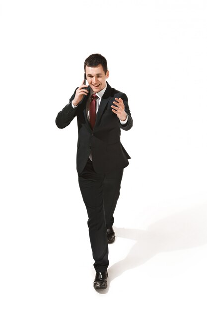 Funny cheerful businessman going with mobile phone over white studio