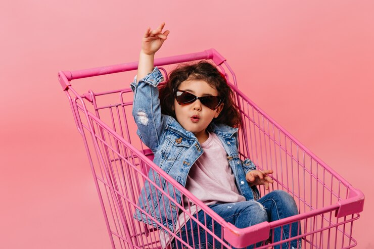Free Photo funny child in sunglasses sitting in shopping cart. studio shot of happy little girl in denim jacket.