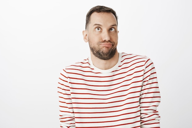 funny childish bearded man in striped pullover, making faces or aping, looking up with squinted eyes and pouting