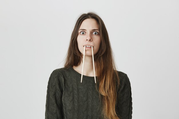 Funny childish woman put chopsticks into mouth, imitating fangs