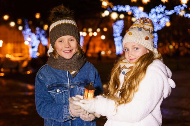 子供たちの女の子と男の子の面白いカップルは、クリスマスのliを背景に彼らの手でランタンを保持しています...