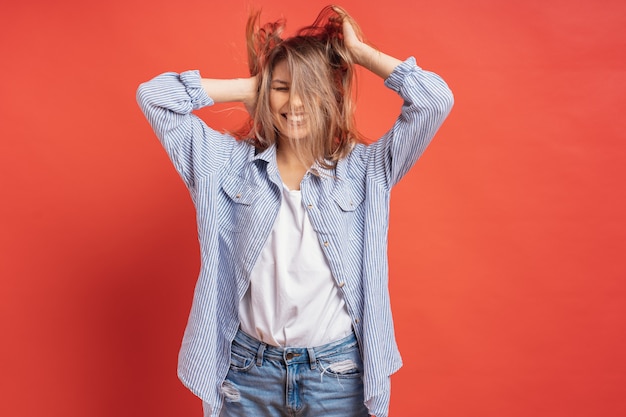 Funny, cute girl having fun while playing with hair isolated on a red wall