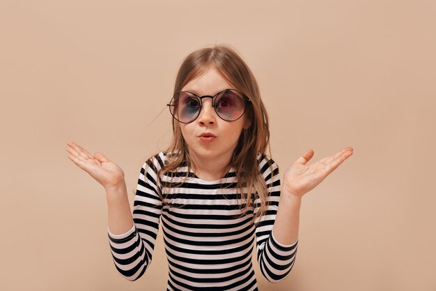 Funny cute little girl 6 years old posing at camera over beige background with surprised true emotions