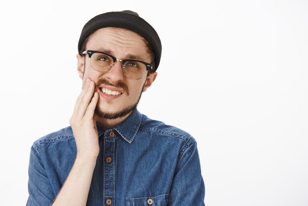 funny displeased bearded male feeling discomfort grimacing looking up and frowning from painful toothache holding hand on cheek and complaining on pain