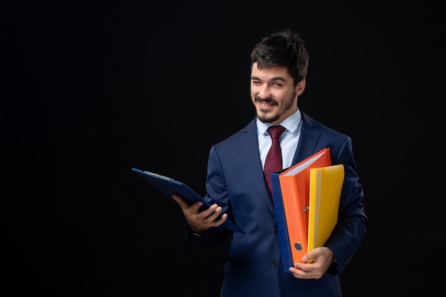 Funny emotional adult in suit holding several documents on isolated dark wall