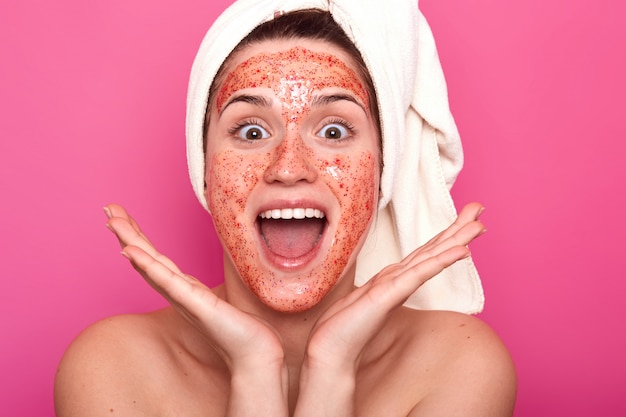 Free photo funny emotional young woman shouts with satisfaction, putting her hands near head, opening mouth and eyes widely, having white towel coned on hair, looks delighted. beauty and skincare concept.