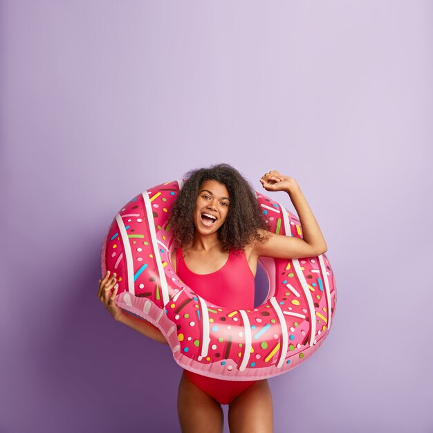 Free photo funny energetic young woman with curly hair posing with pool floaty