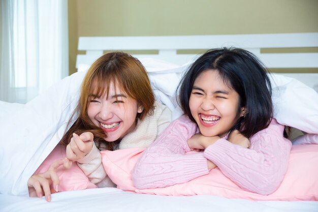 funny friends lying under blanket with pillows on bed