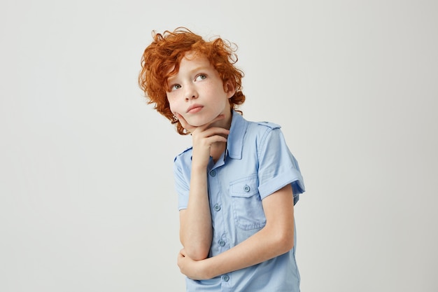 Funny ginger little boy with wavy hair and freckles dreamy looking aside trying to remember