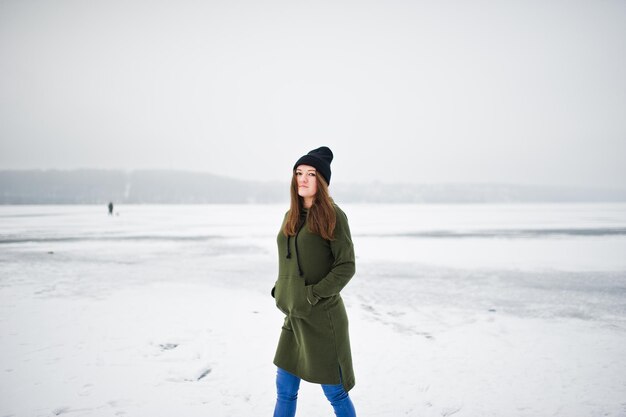 겨울날 얼어붙은 호수에서 긴 녹색 운동복 청바지와 검은색 모자를 쓴 재미있는 소녀