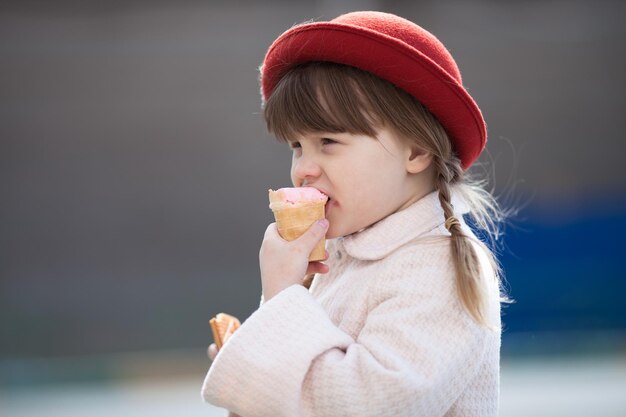 Funny girl with pigtails in hat eating ice cream